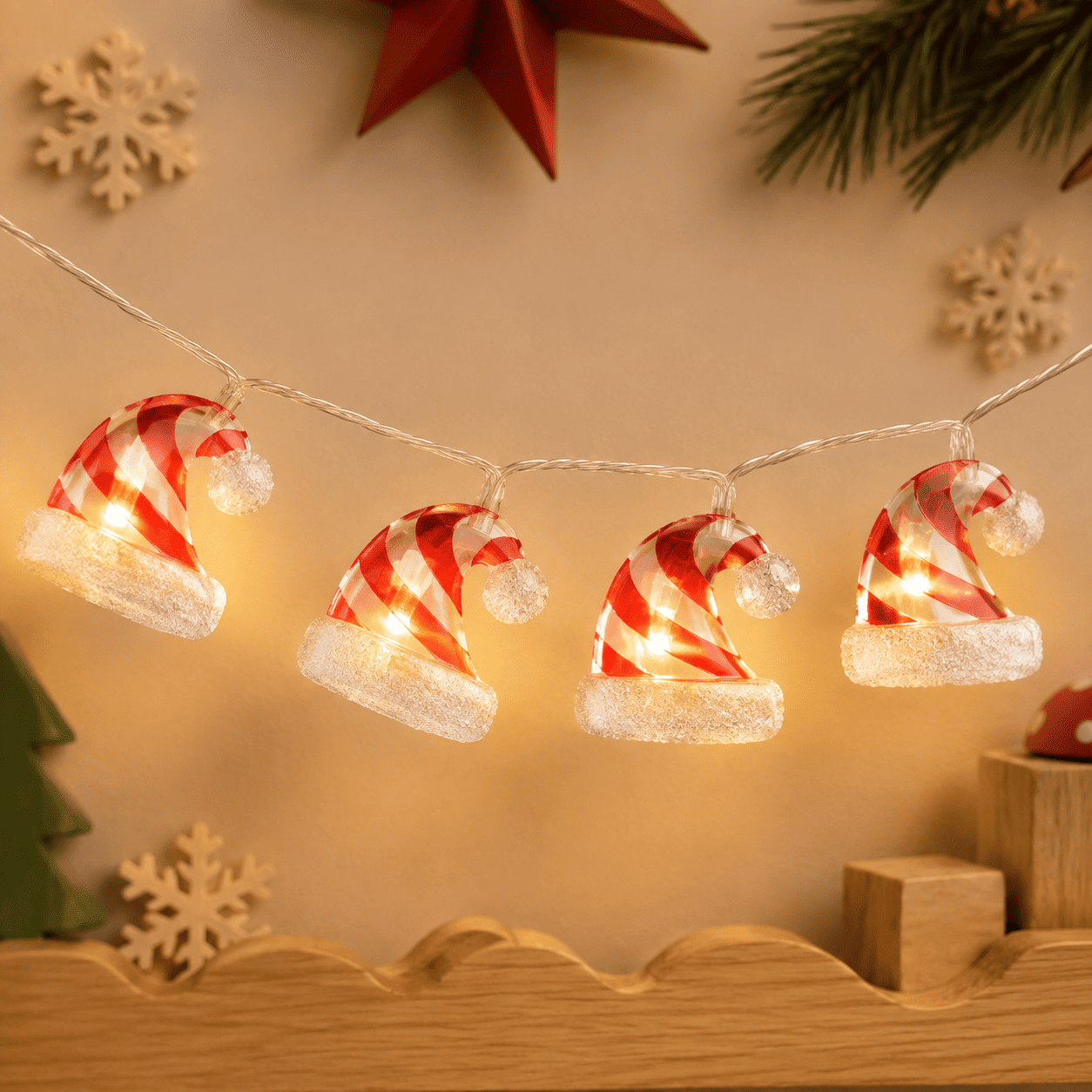Guirlande lumineuse de Noël à bonnets rouges et blancs rayés avec pompons blancs, sur un mur beige.