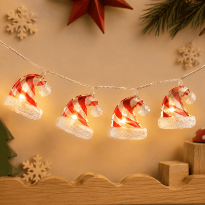 Guirlande lumineuse de Noël à bonnets rouges et blancs rayés avec pompons blancs, sur un mur beige.