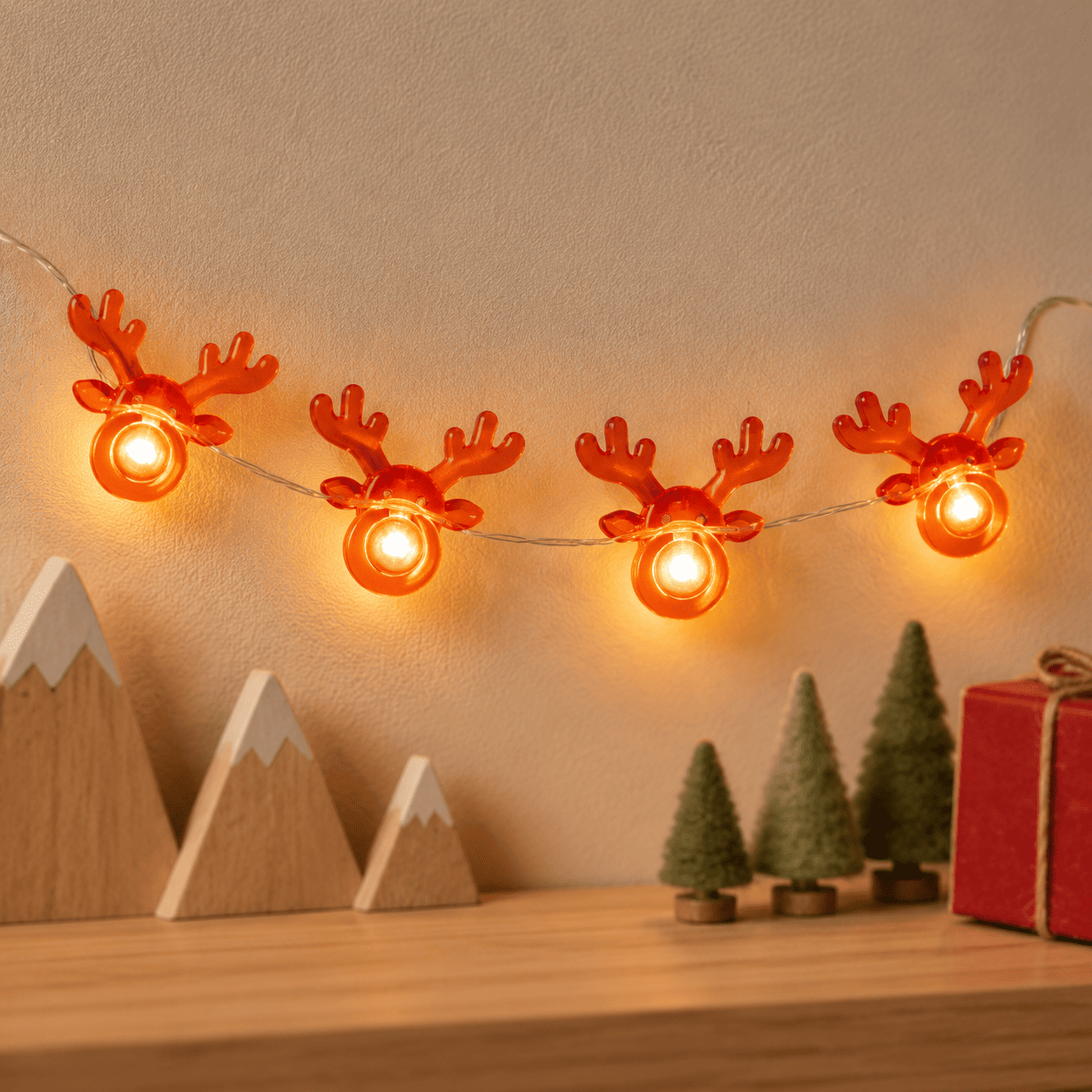 Guirlande lumineuse de Noël à têtes de renne rouges, allumée sur un mur beige dans un décor en bois.