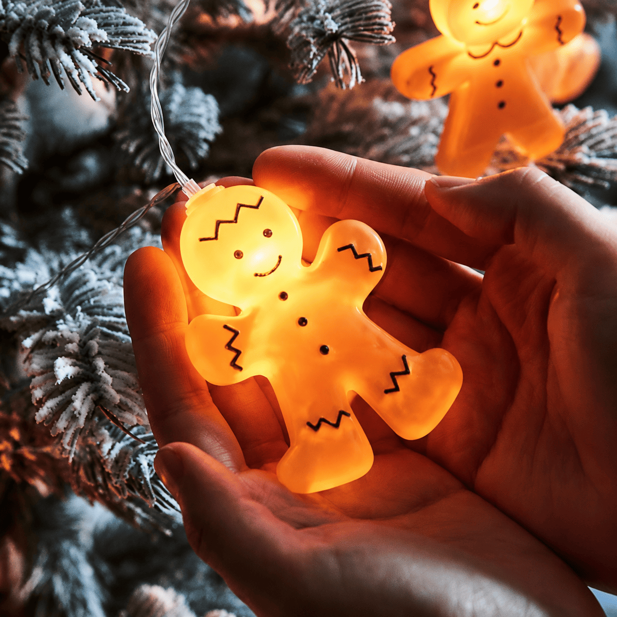 Pain d’épices lumineux de guirlande tenu dans les mains devant un sapin enneigé